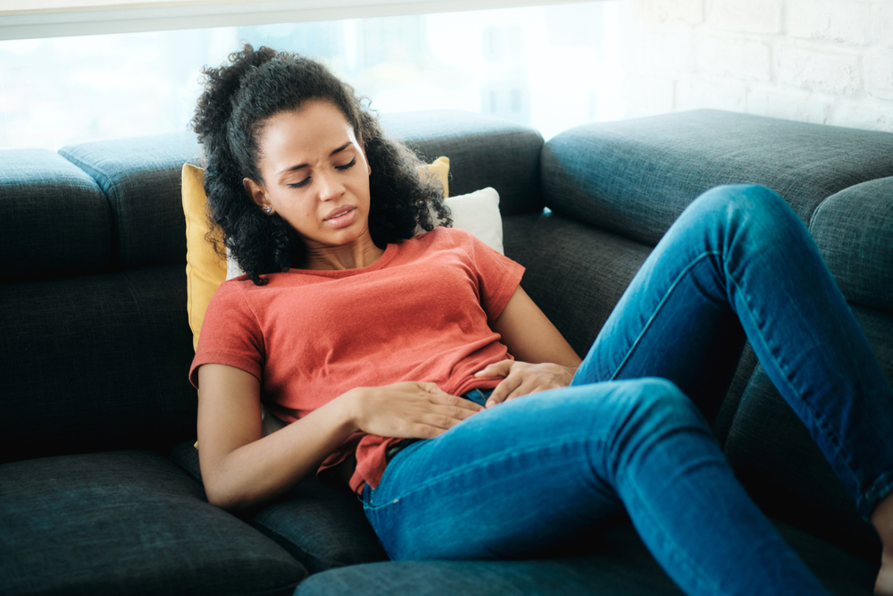 Young woman with menstrual pain lying on the sofa
