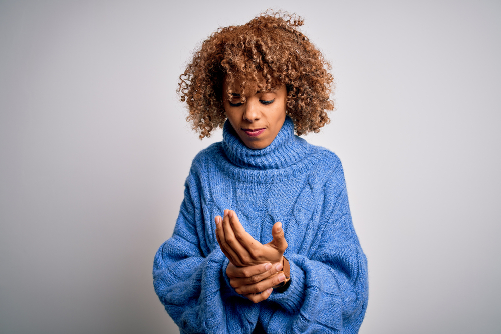 Black woman wearing a sweater and rubbing her hands